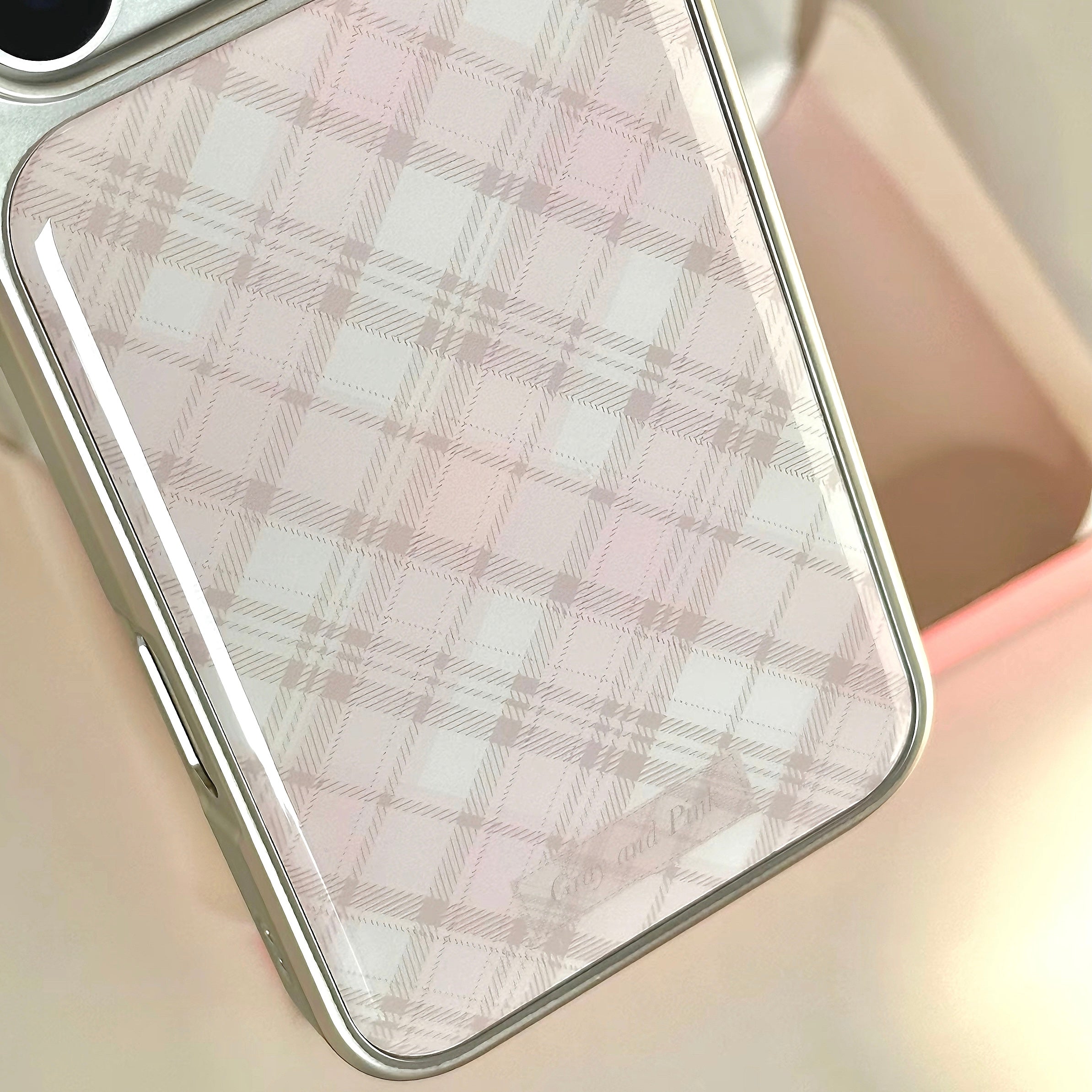 A close-up of a phone case with a pale pink and white plaid pattern, shown resting on a soft beige surface.