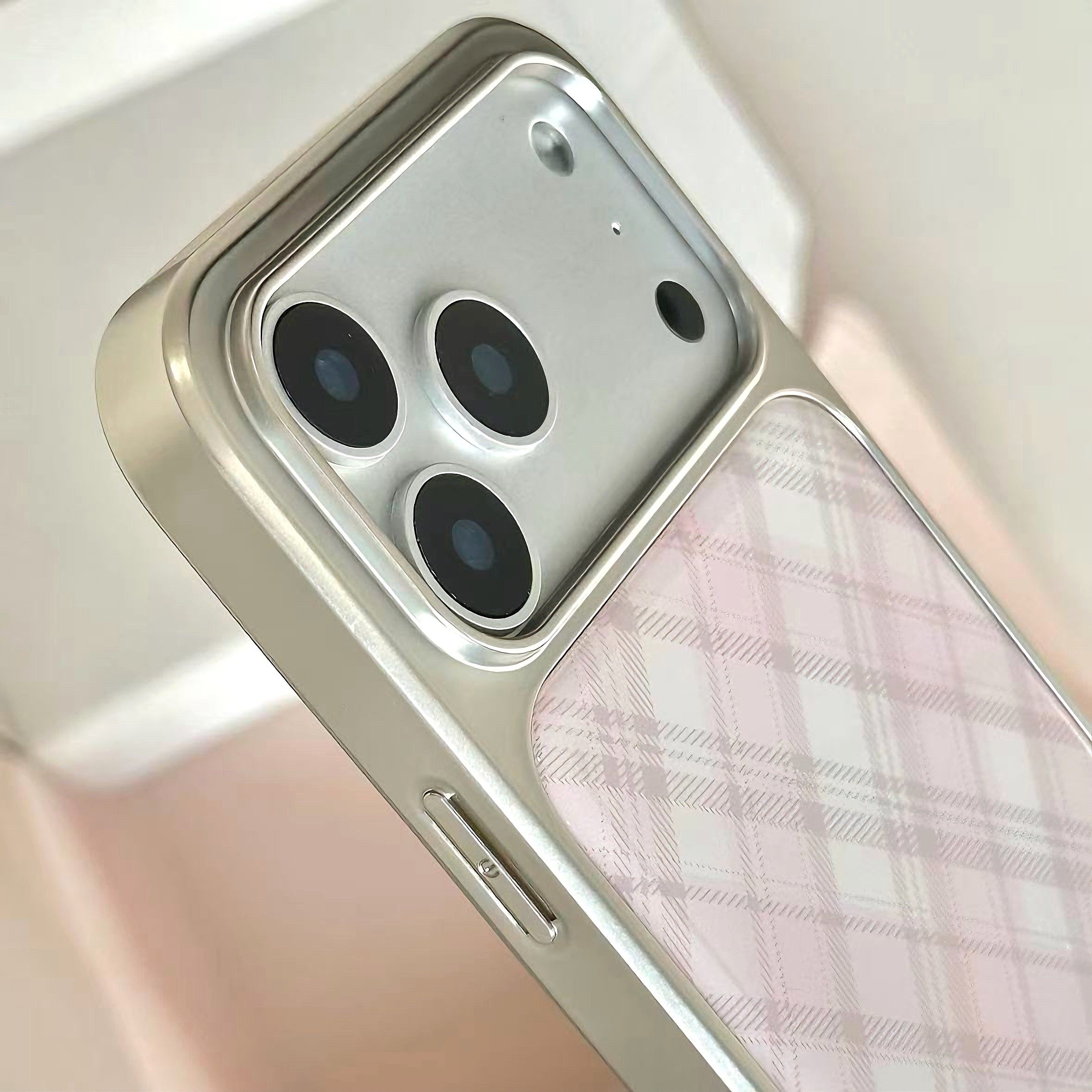 Close-up of a smartphone case mounted on a phone, showing a metallic silver bumper around the camera area and a pale pink plaid pattern on the back.
